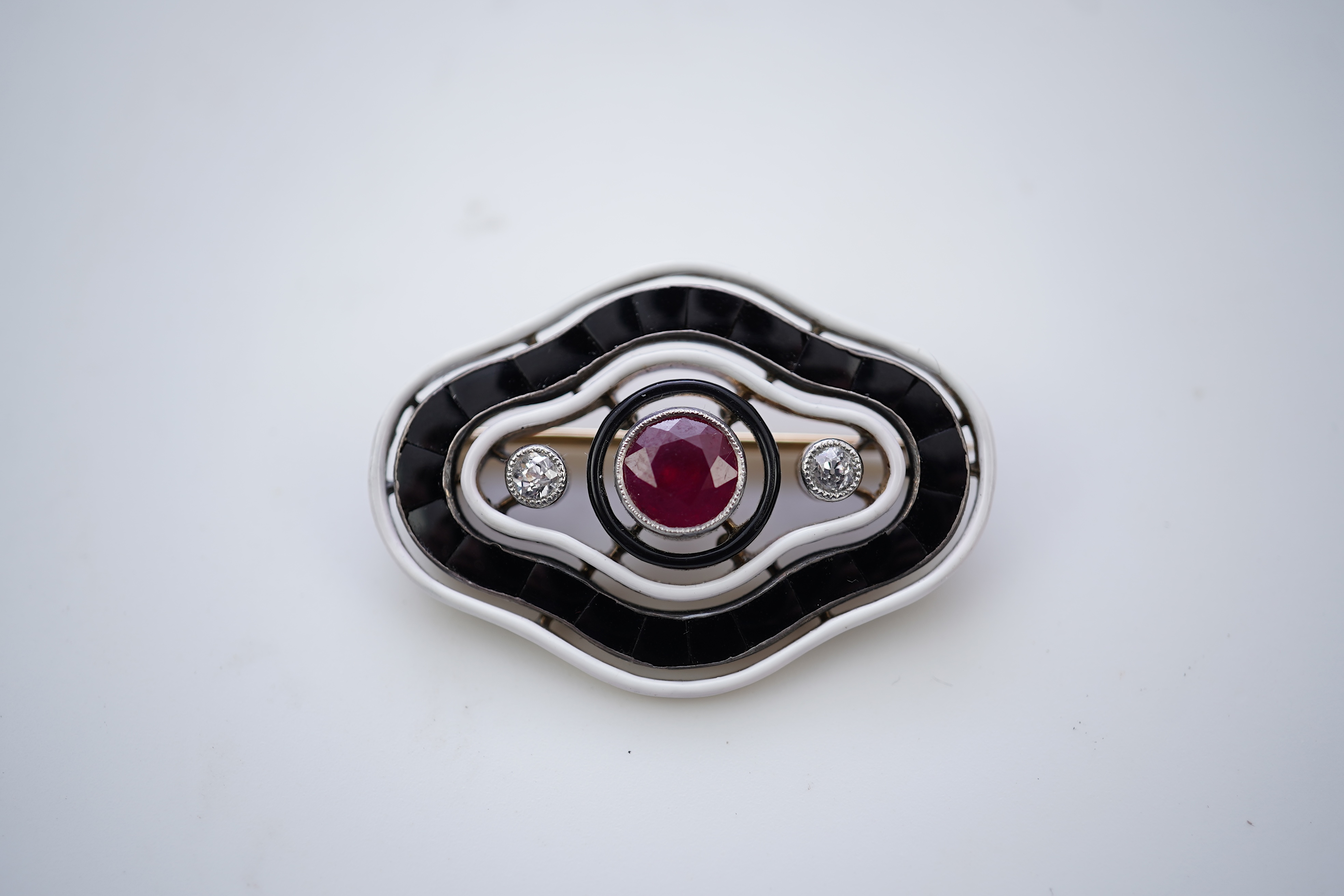 An unusual Art Deco onyx, enamel, ruby and diamond brooch, circa 1920